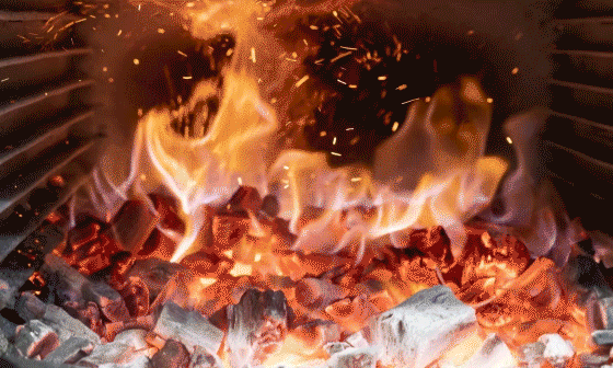 Feu de charbon de bois incandescent avec des flammes, des étincelles et de la fumée dans un gril.