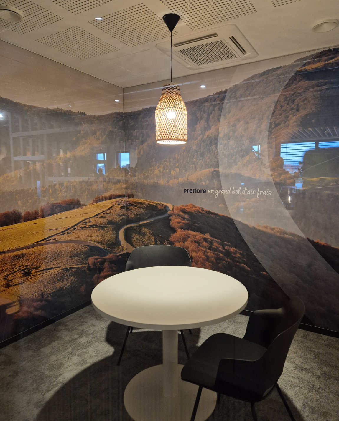 Round white table with two black chairs in front of a landscape mural. A pendant light hangs above the table.
