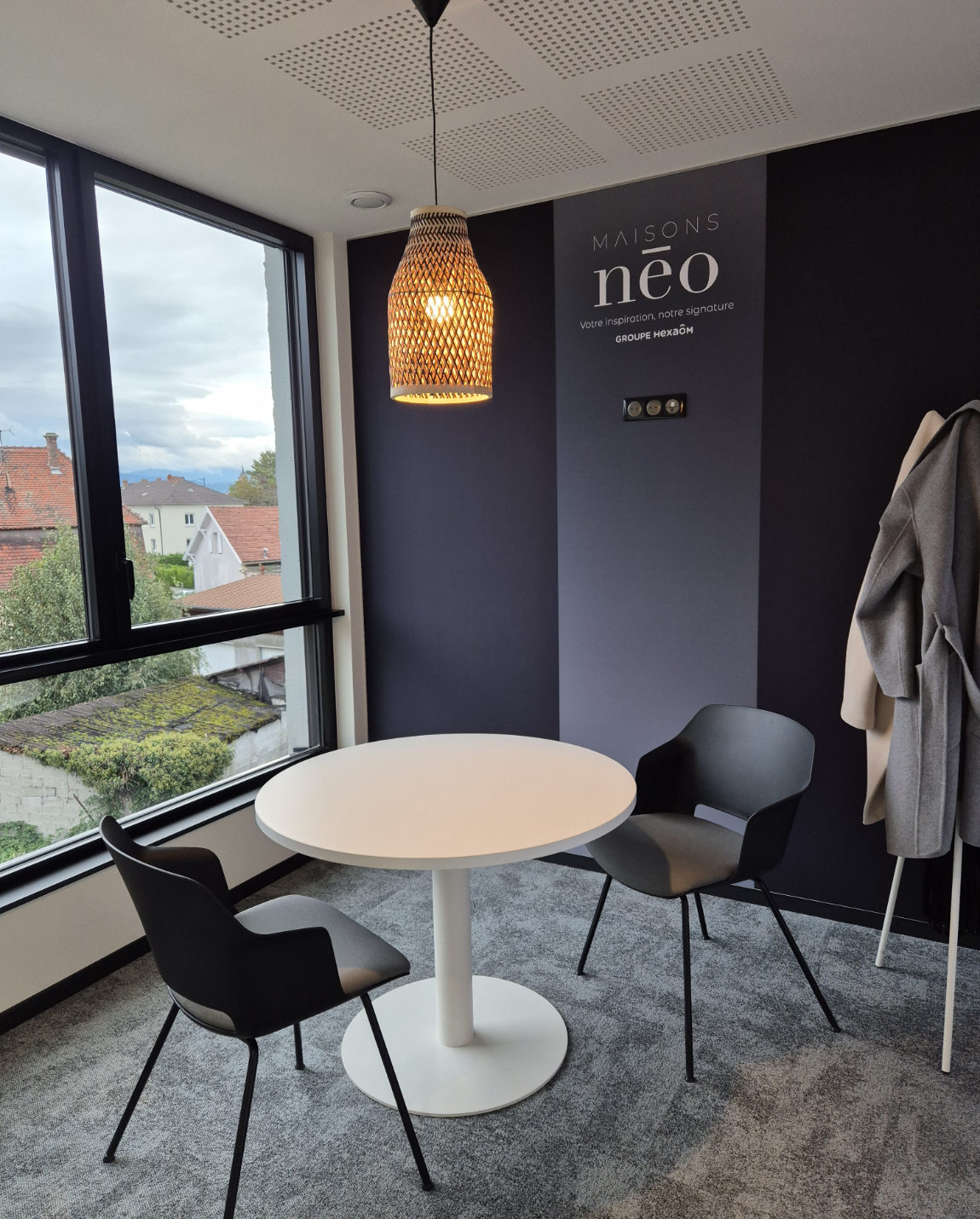 Meeting area with round white table, two chairs, dark accent wall, window, and patterned light fixture.