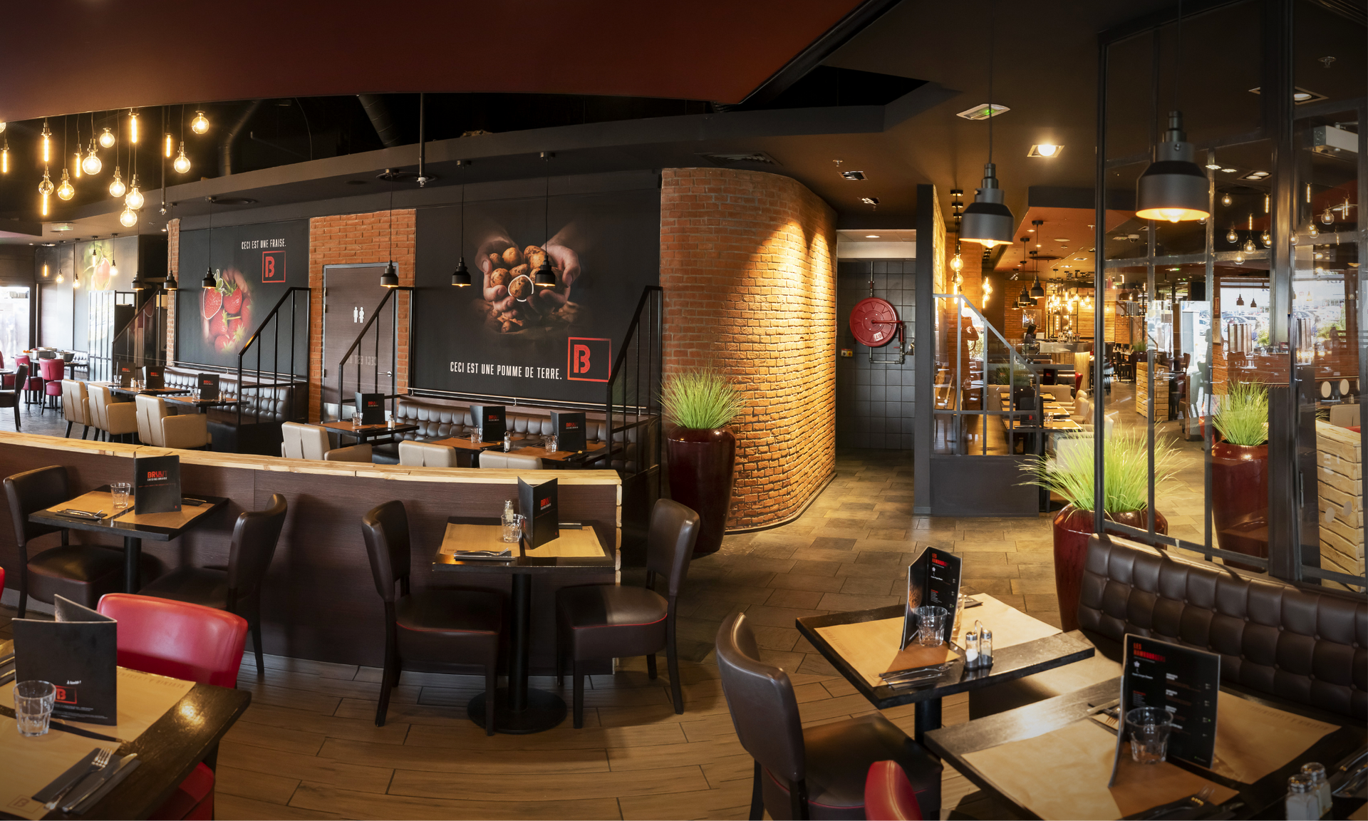 Interior view of a modern restaurant with tables, chairs, dark walls, and brick accents.