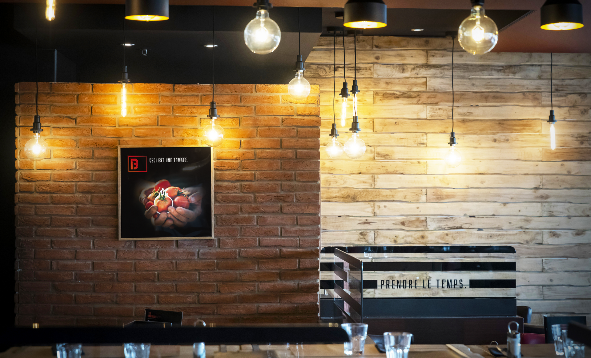 Restaurant interior: brick wall, wooden wall, hanging lights, framed artwork, table setting.