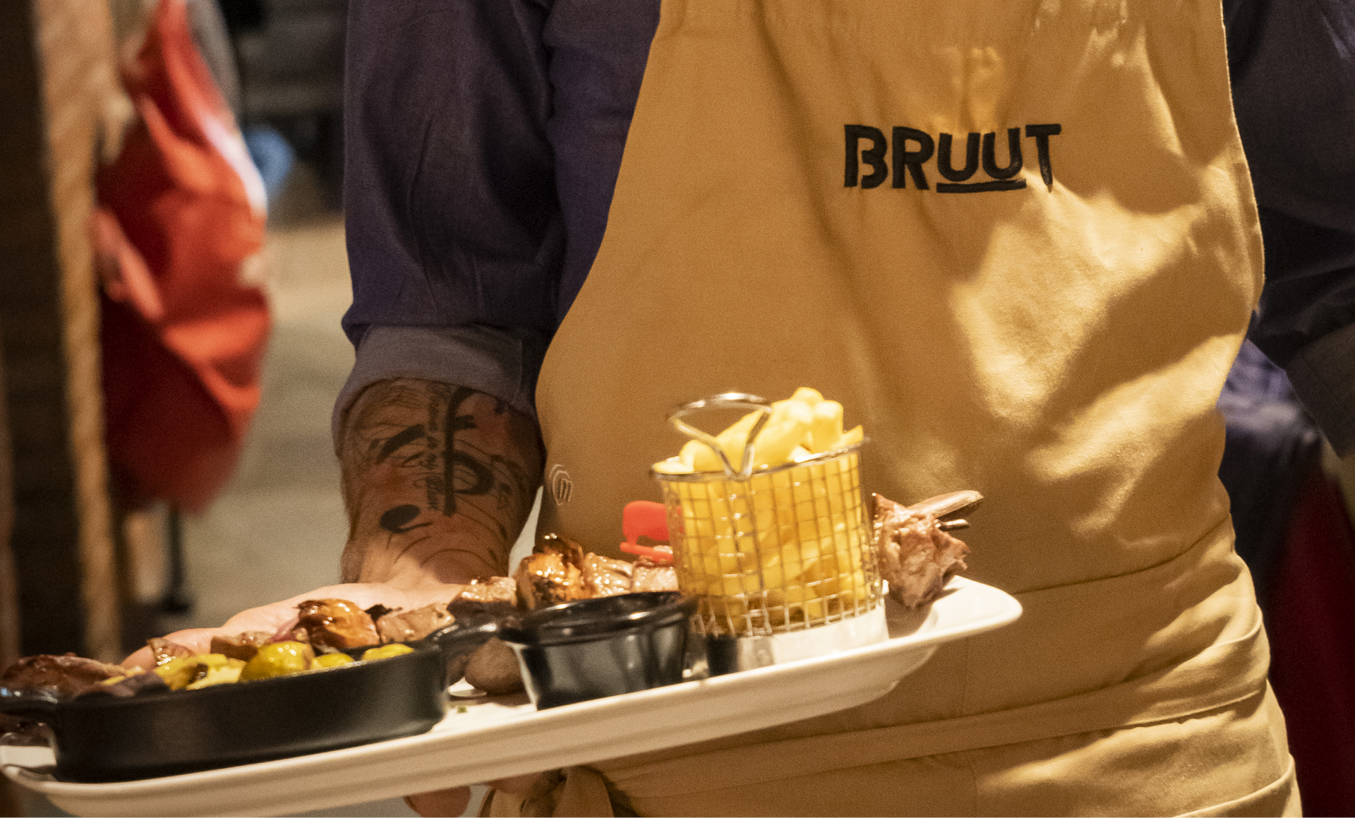 Person holding a tray with food, including fries and meat; wearing a