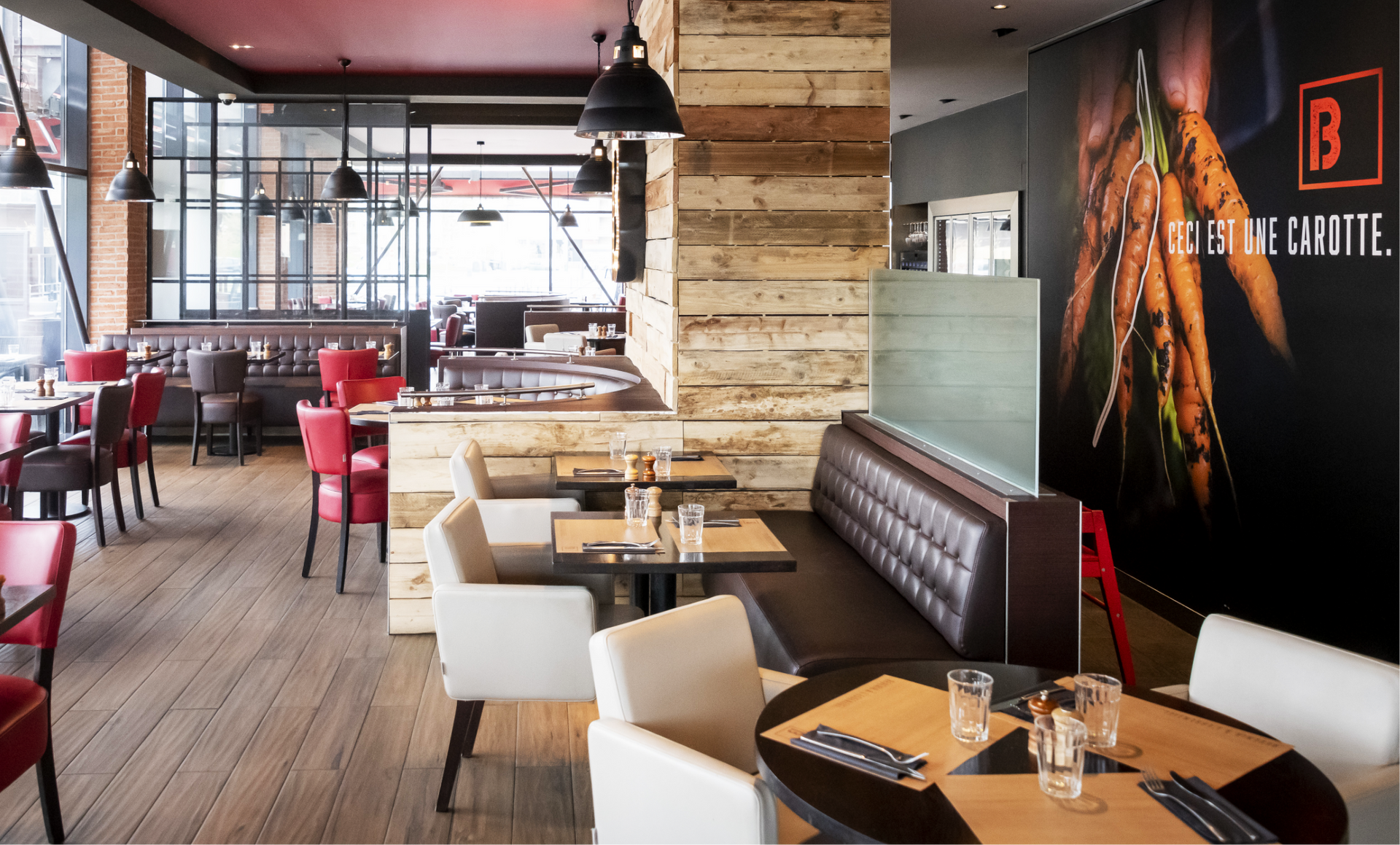 Restaurant interior: wooden floors, red chairs, beige booths, black lamps.