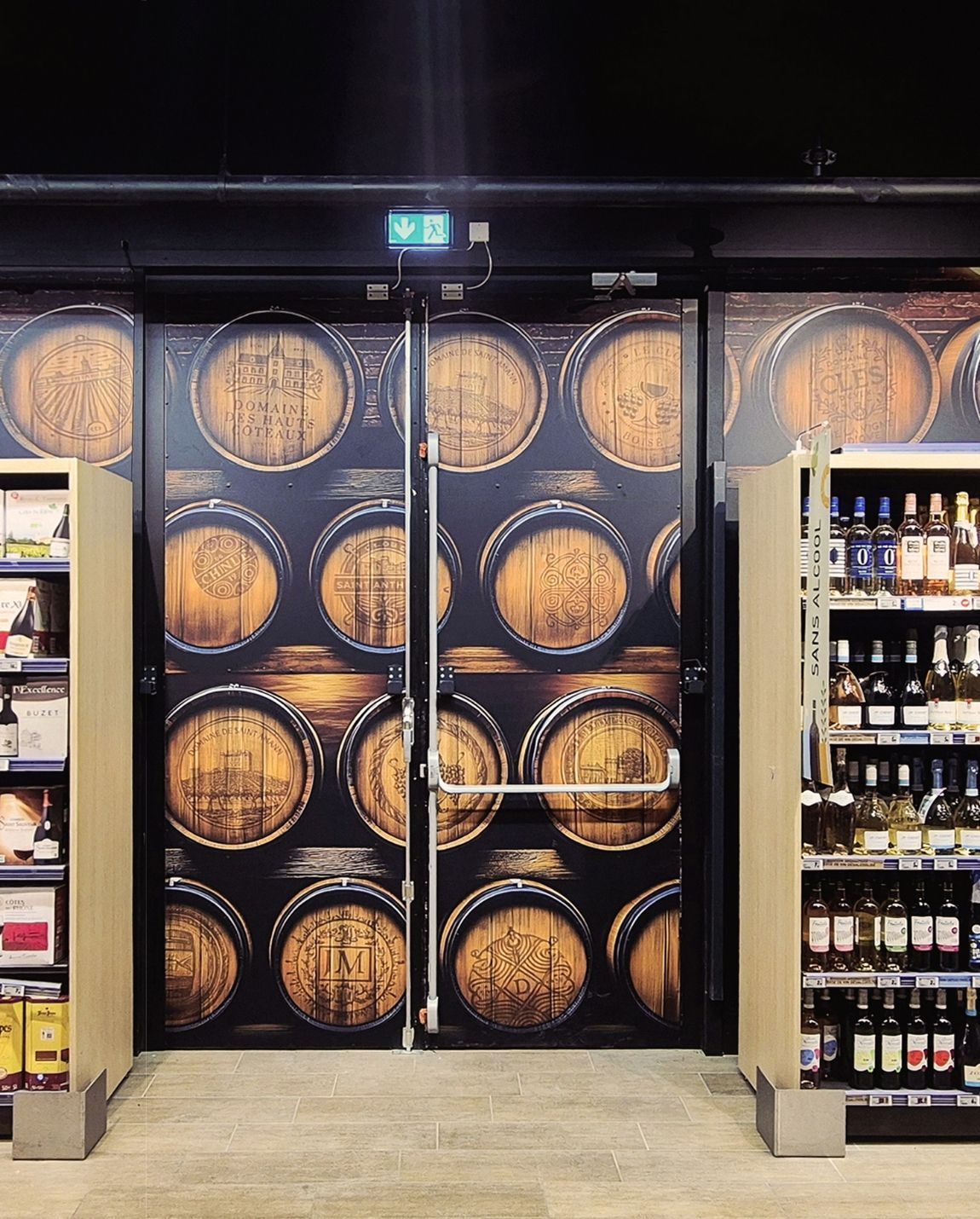 Allée de magasin avec une fresque murale représentant un tonneau noir entre les étagères de produits en bouteille