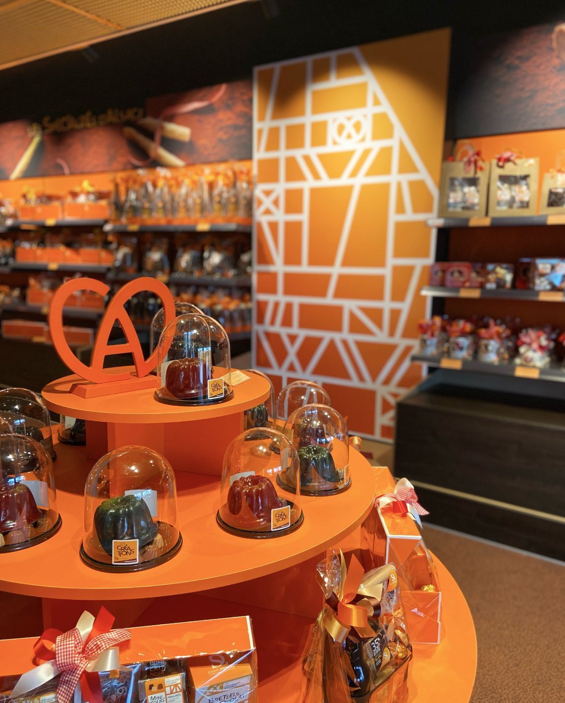 Orange-themed shop display featuring baked goods under glass domes and shelves of packaged products.