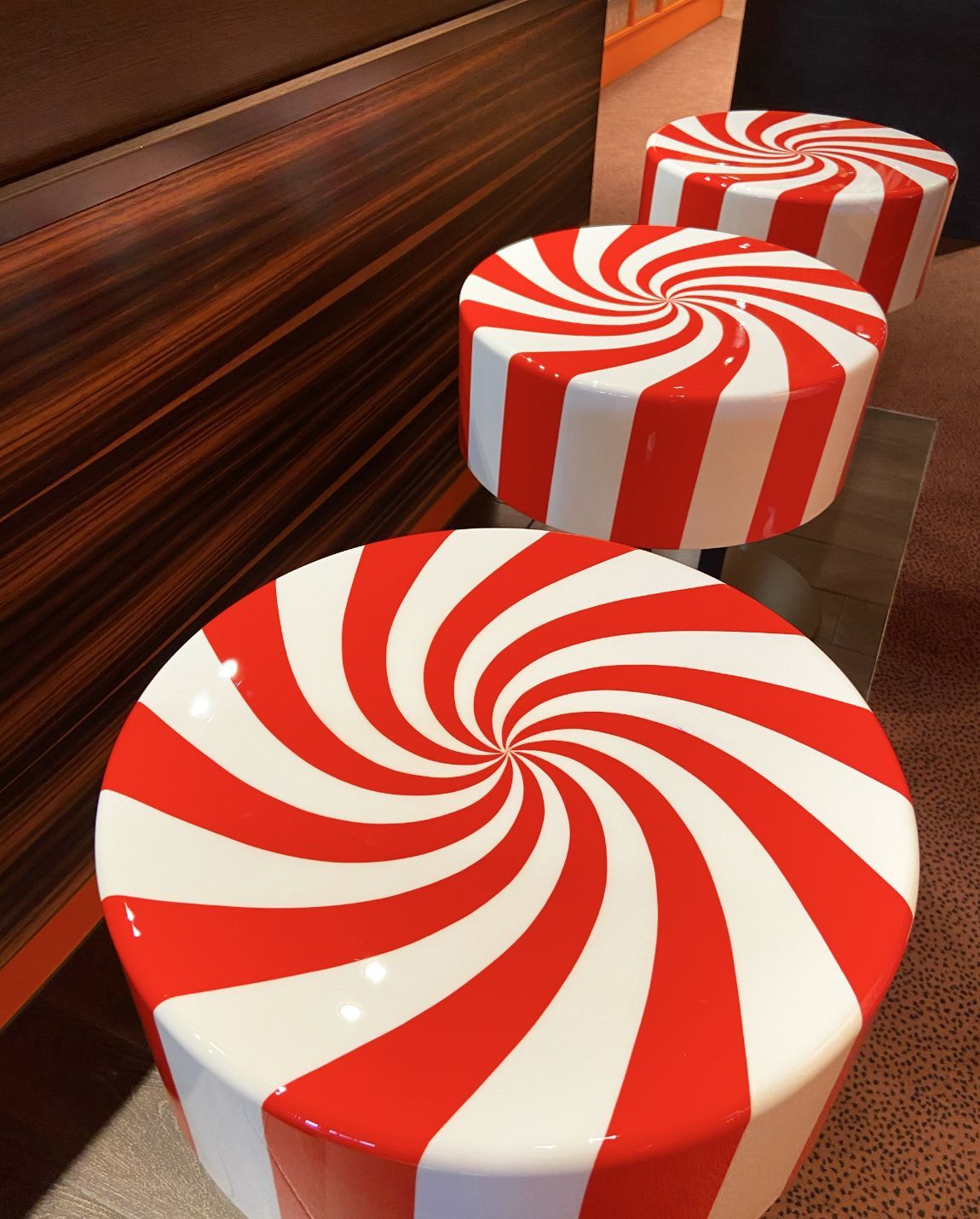 Three red and white peppermint-swirl stools near a wood-paneled wall.