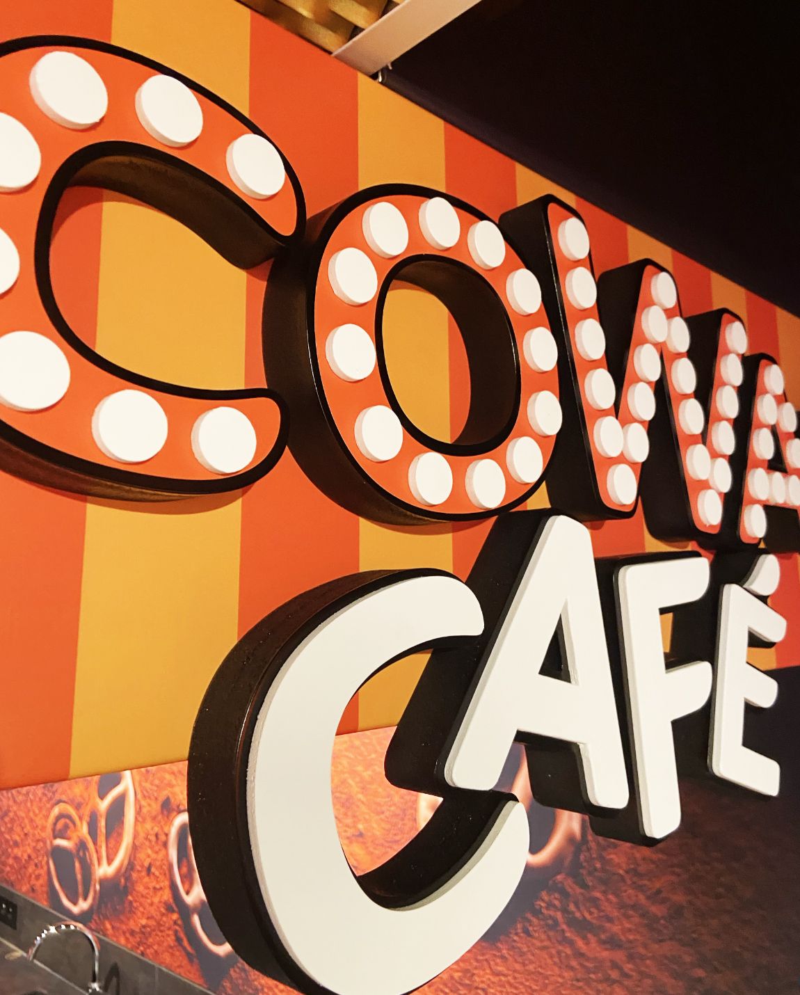 Close-up of a sign for Coma Café with large, 3D letters. Orange and white colors on a striped background.