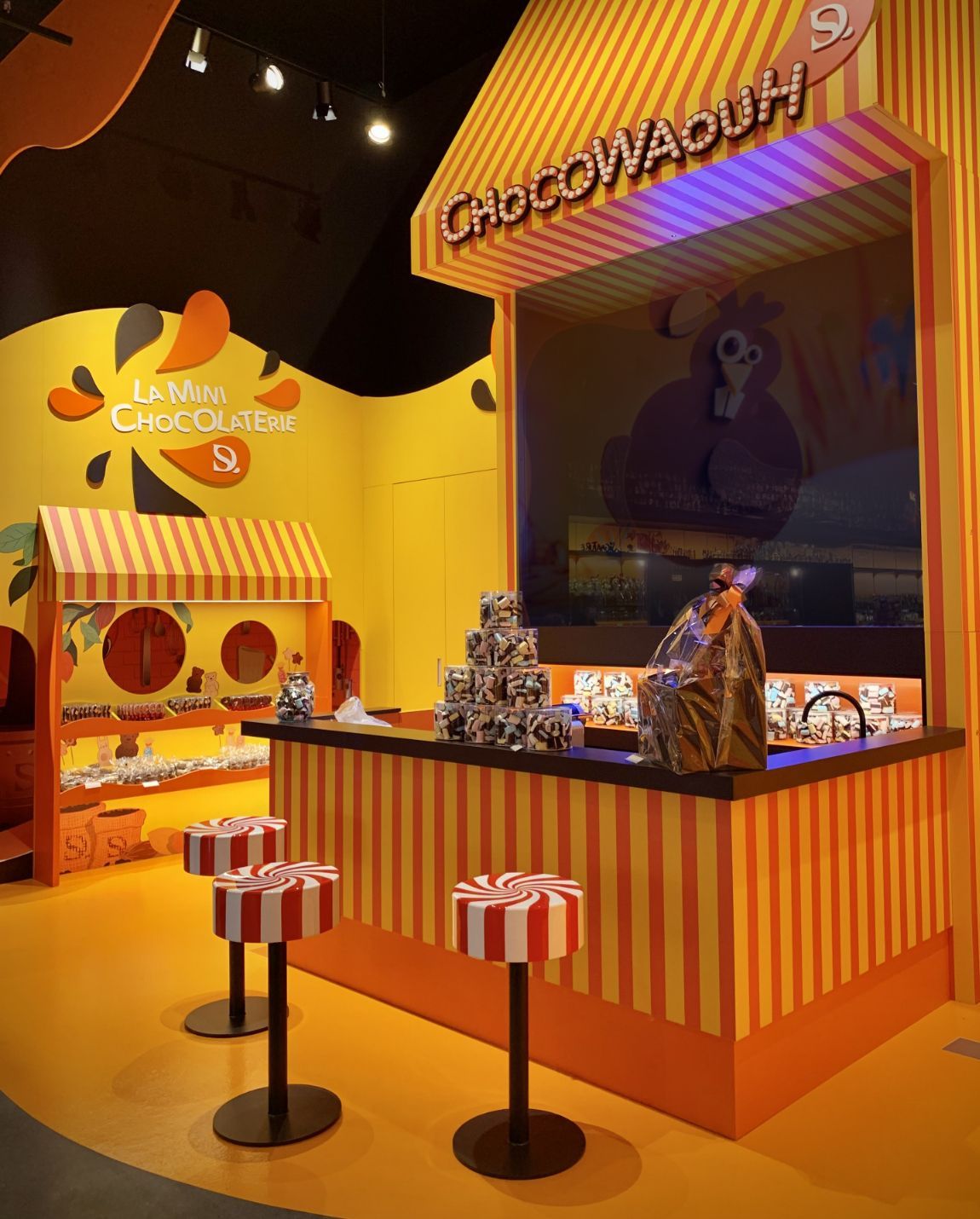 Chocolate shop with orange and yellow striped awning and walls, displaying chocolate.
