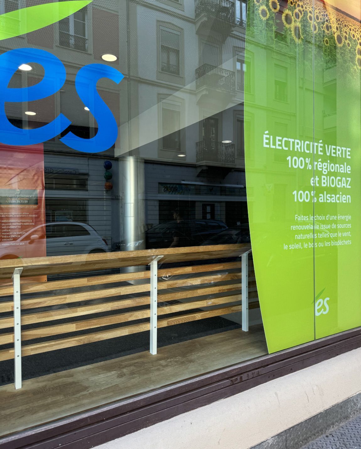 Window display with green and blue text, sunlight reflections, and a wooden rail.