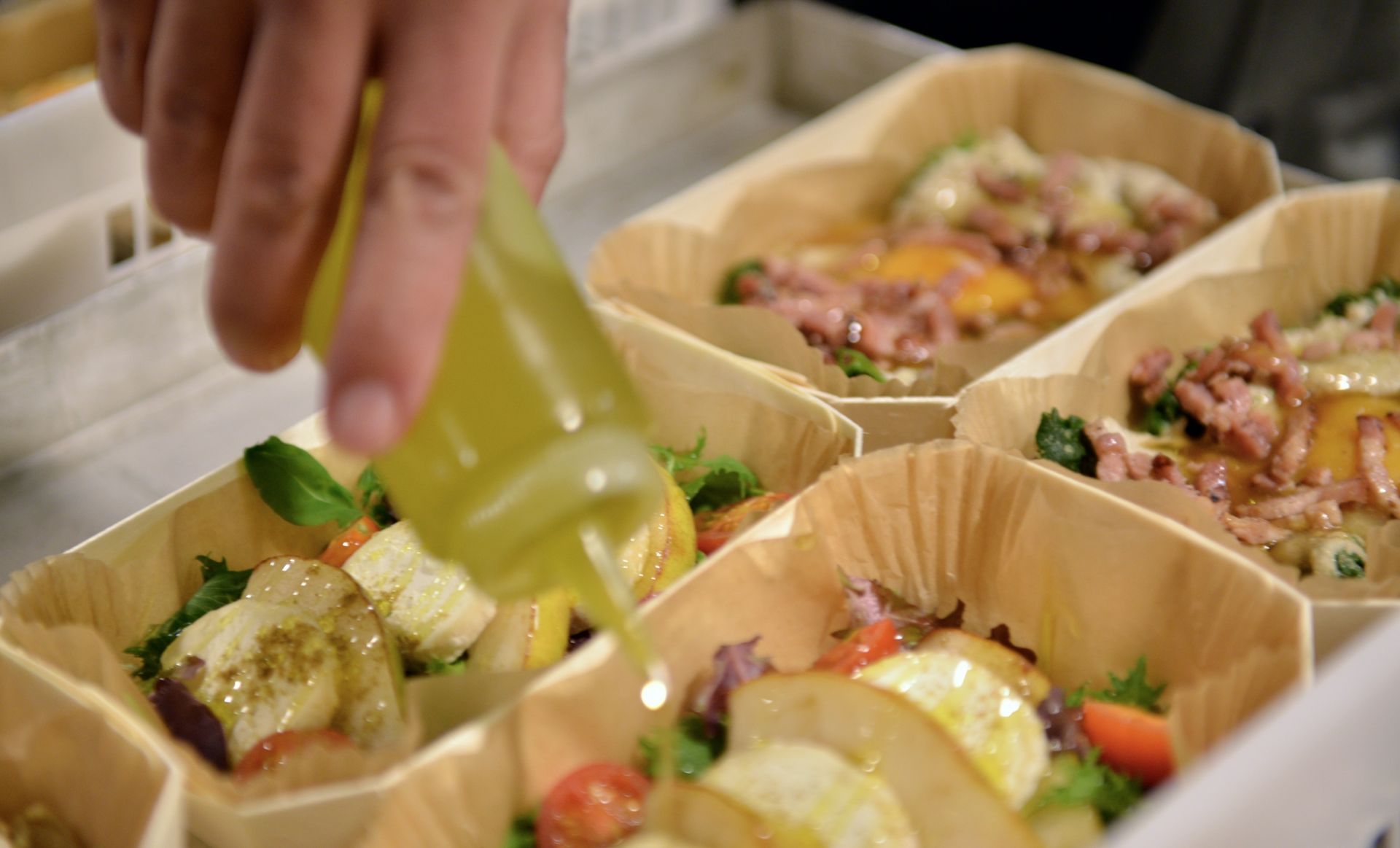 Chef pouring dressing over salads in wooden trays, showcasing various ingredients and textures.