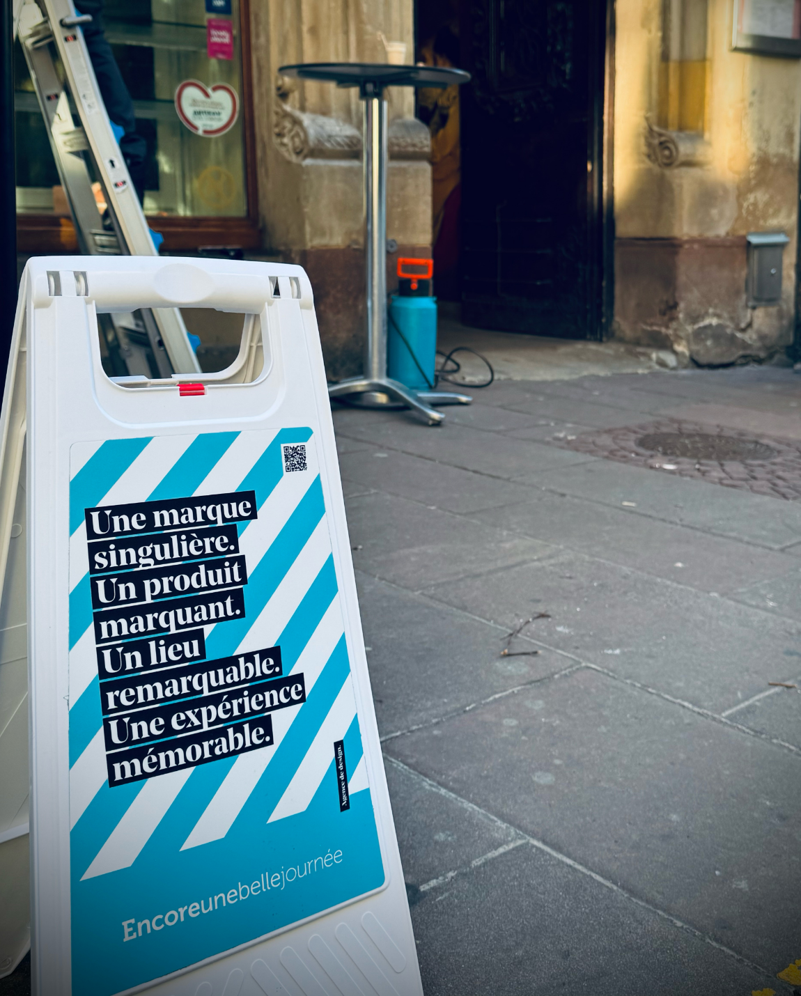 Panneau blanc et bleu sur le trottoir : « Une marque singulière… ». 