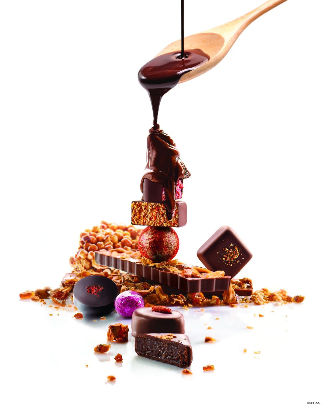 Dark chocolate being poured over a tower of chocolates and treats, on a white background.