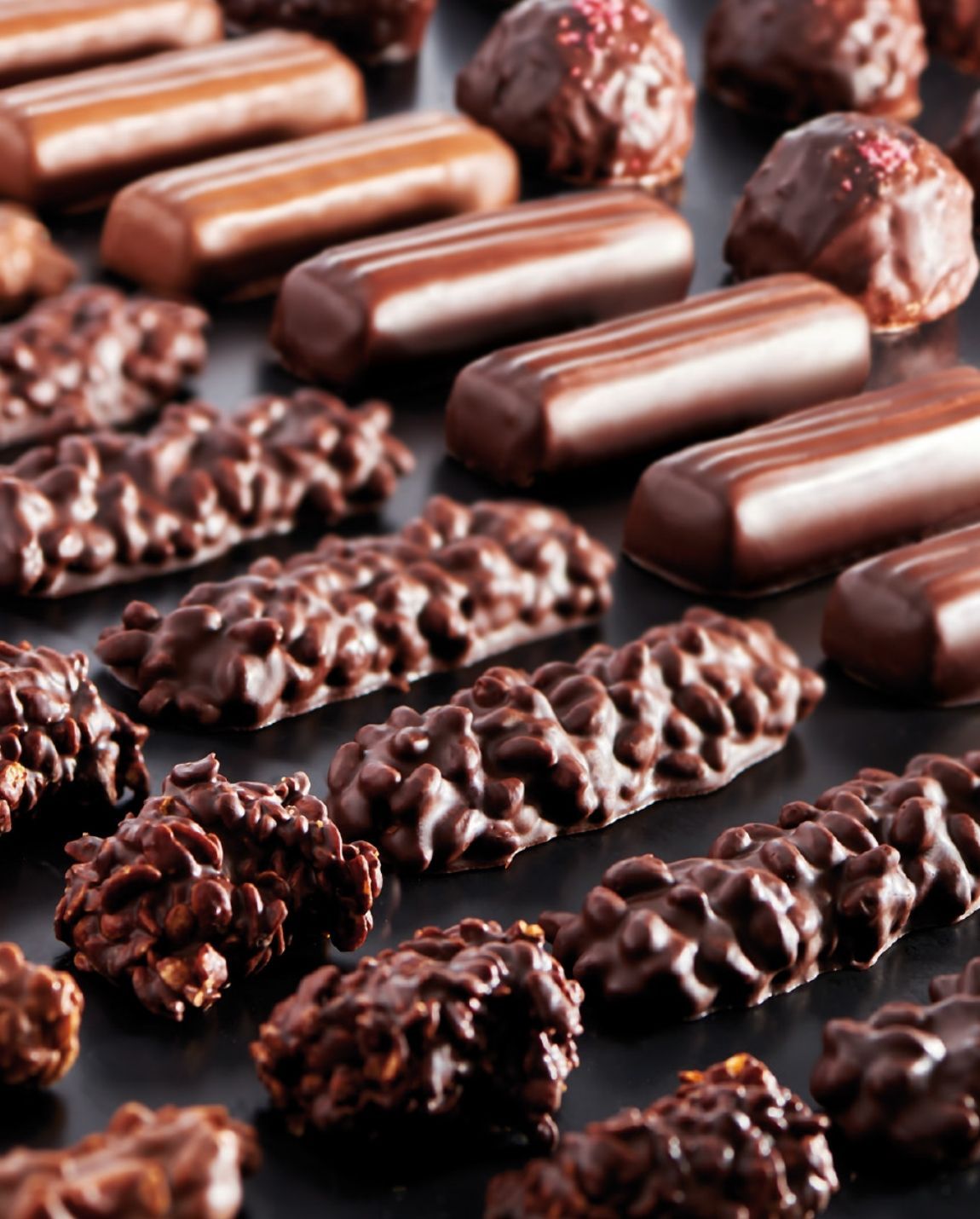 Close-up of assorted chocolates, including bars and truffle-like candies, on a dark surface.