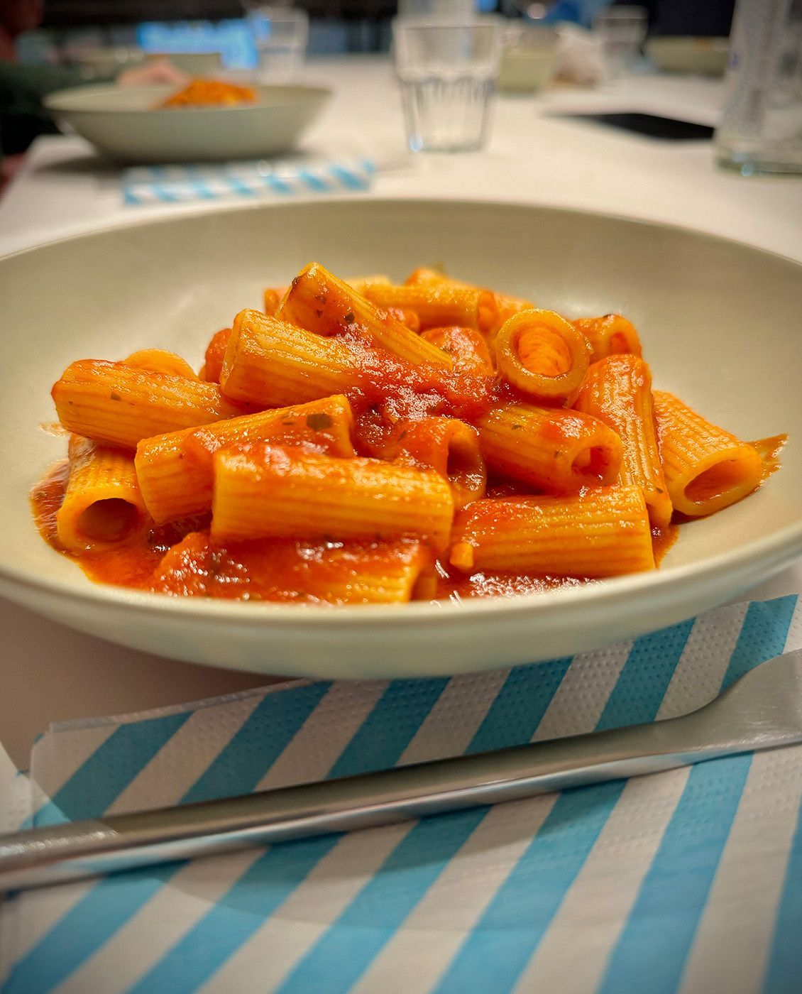 Pâtes rigatoni à la sauce tomate servies dans un bol blanc, sur une serviette à rayures bleues et blanches.
