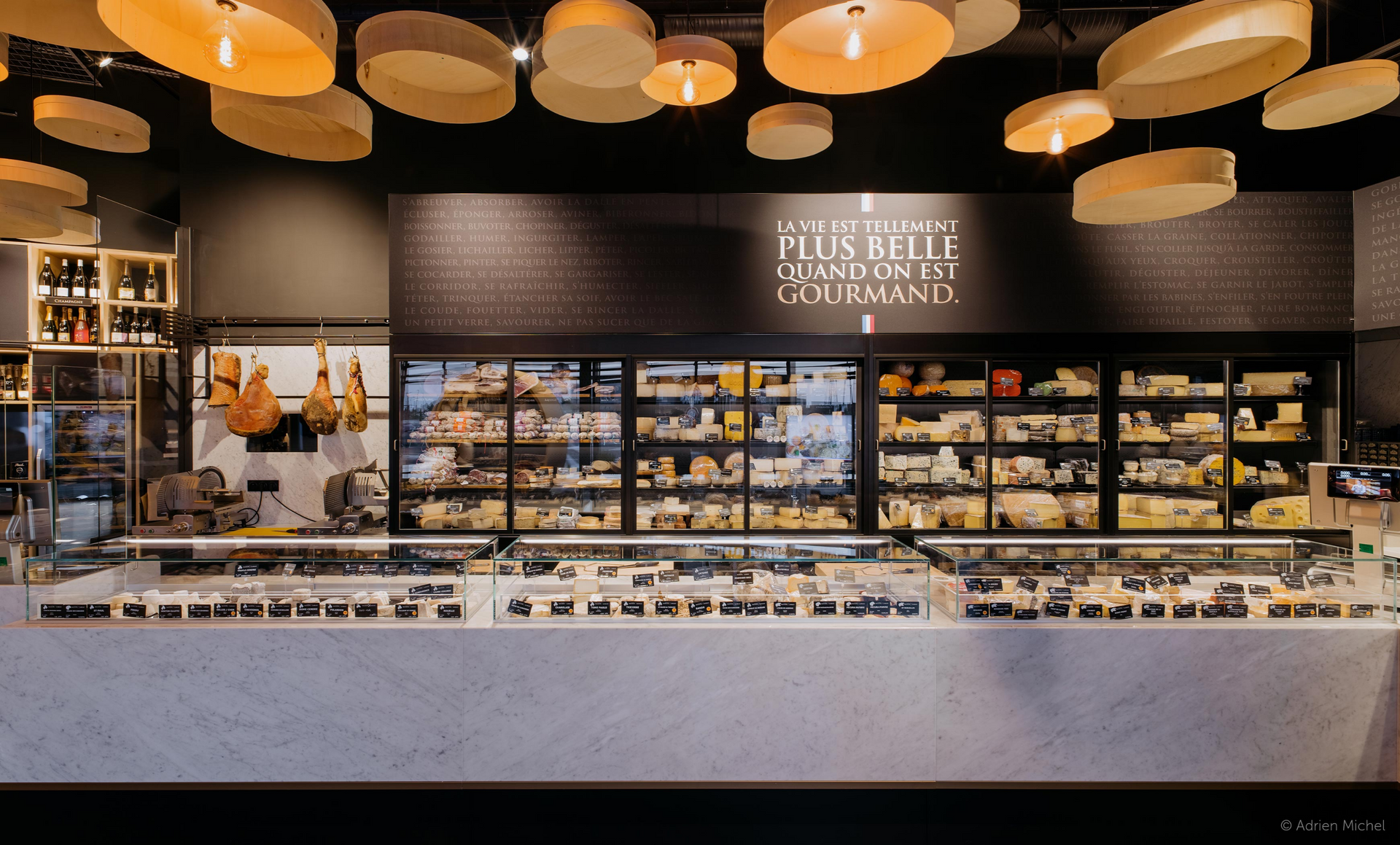 Intérieur de fromagerie avec longue vitrine, accents noirs et blancs et éclairage chaleureux.