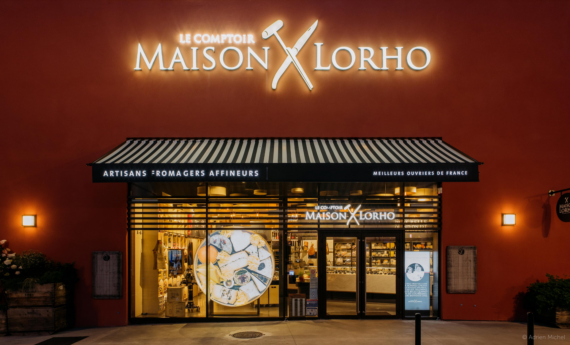 Exterior of Le Comptoir Maison Lorho restaurant, red facade, illuminated sign, glass windows.