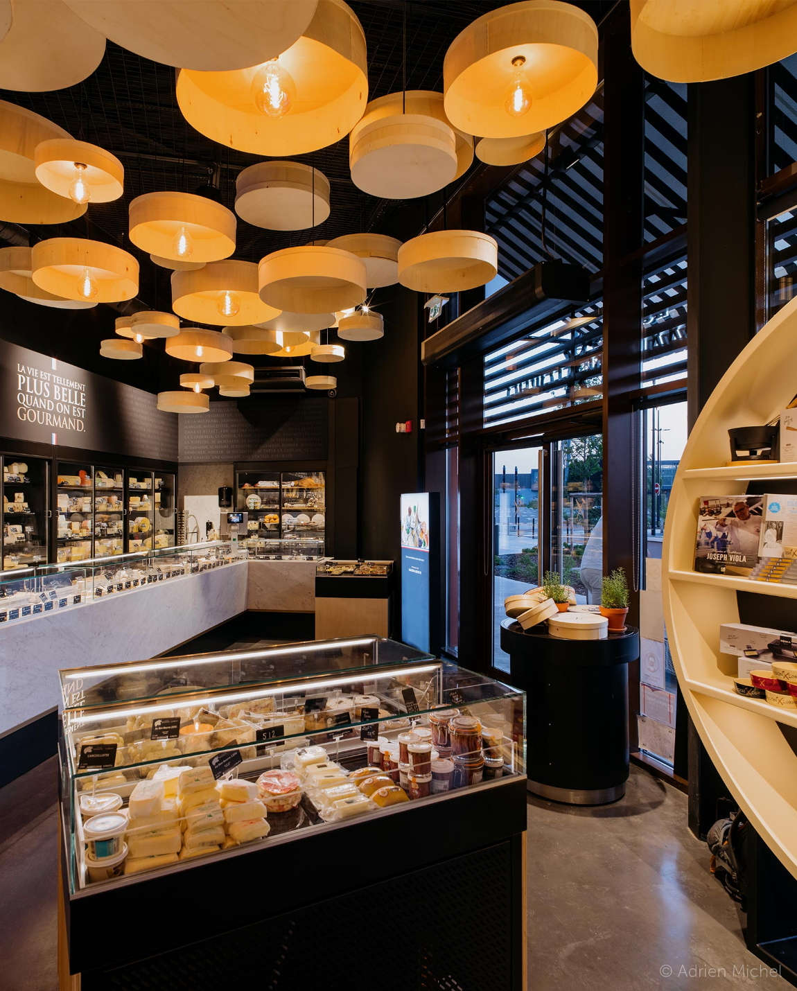 Cheese shop interior with display cases, hanging circular lights, dark walls, and an open doorway.