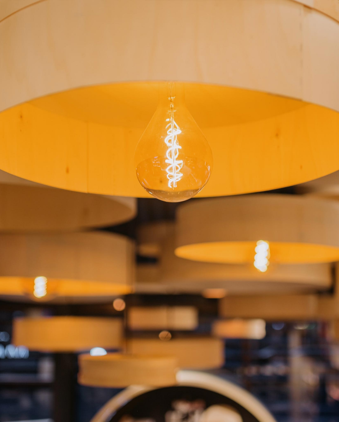 Yellow light bulb hanging from a wooden lamp shade, others blurred in the background.