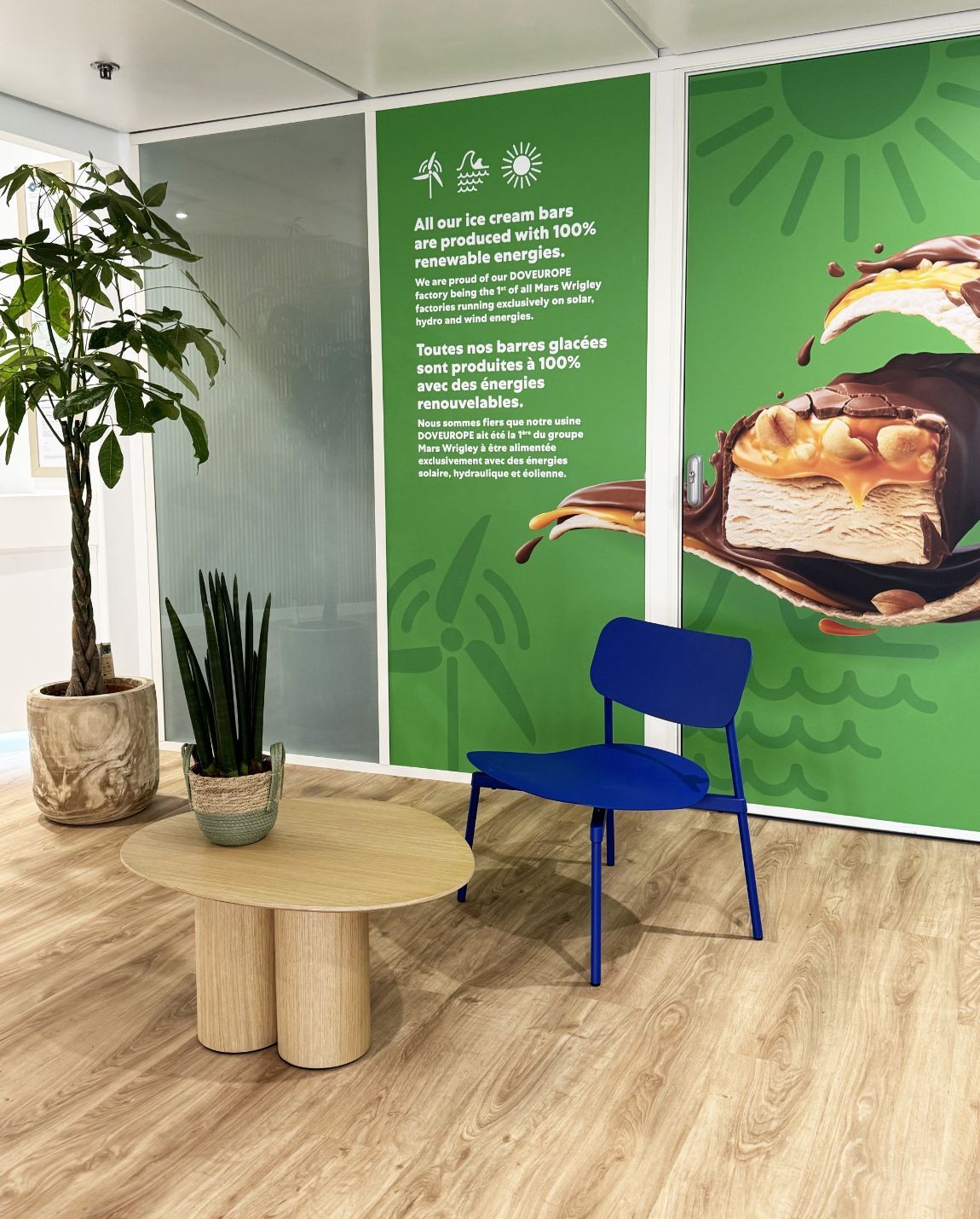 Interior with a blue chair, small table with plants, and a green backdrop with a dessert image.