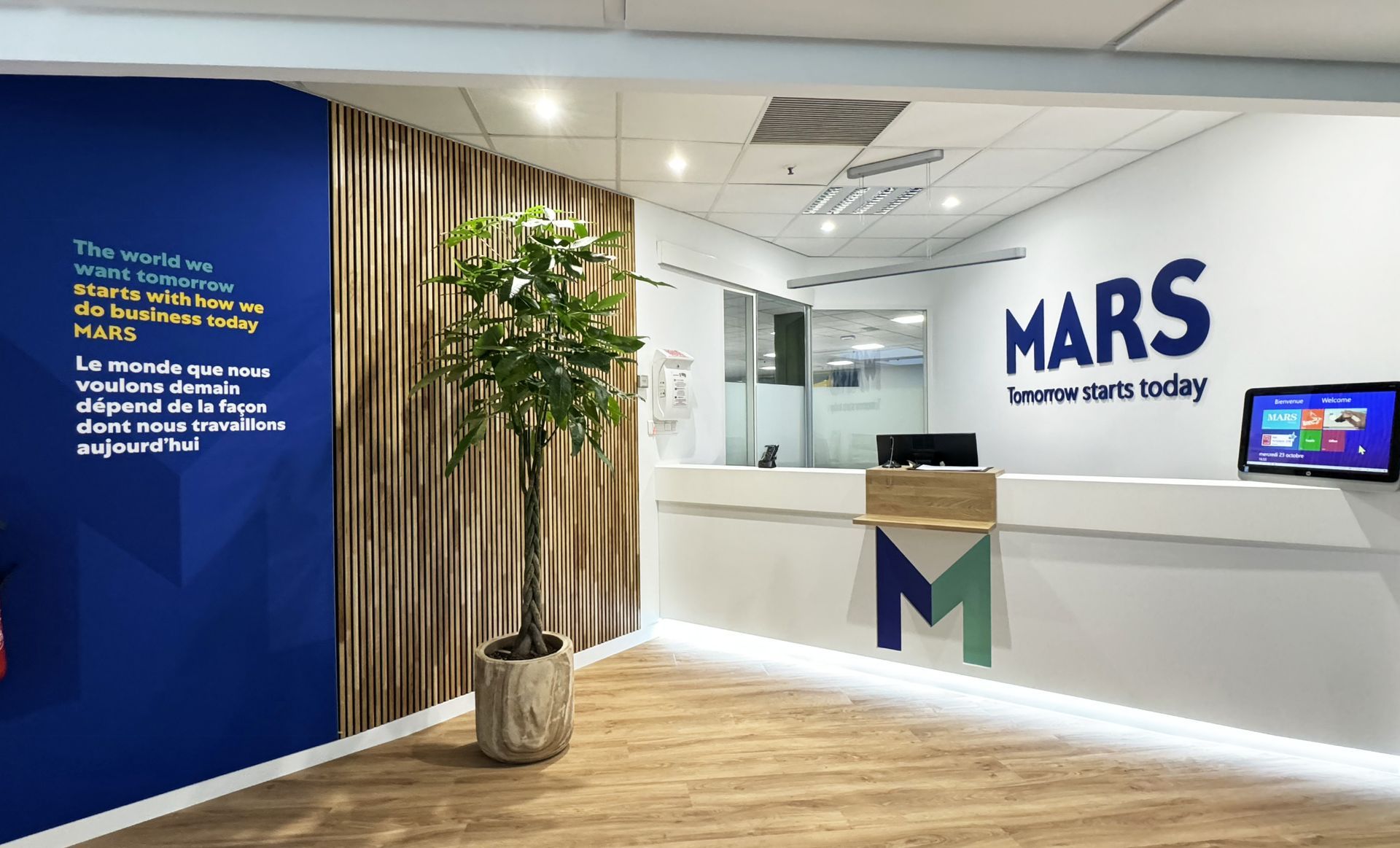 Reception area of Mars company; wood paneling, blue accent wall, plant, and MARS logo visible.