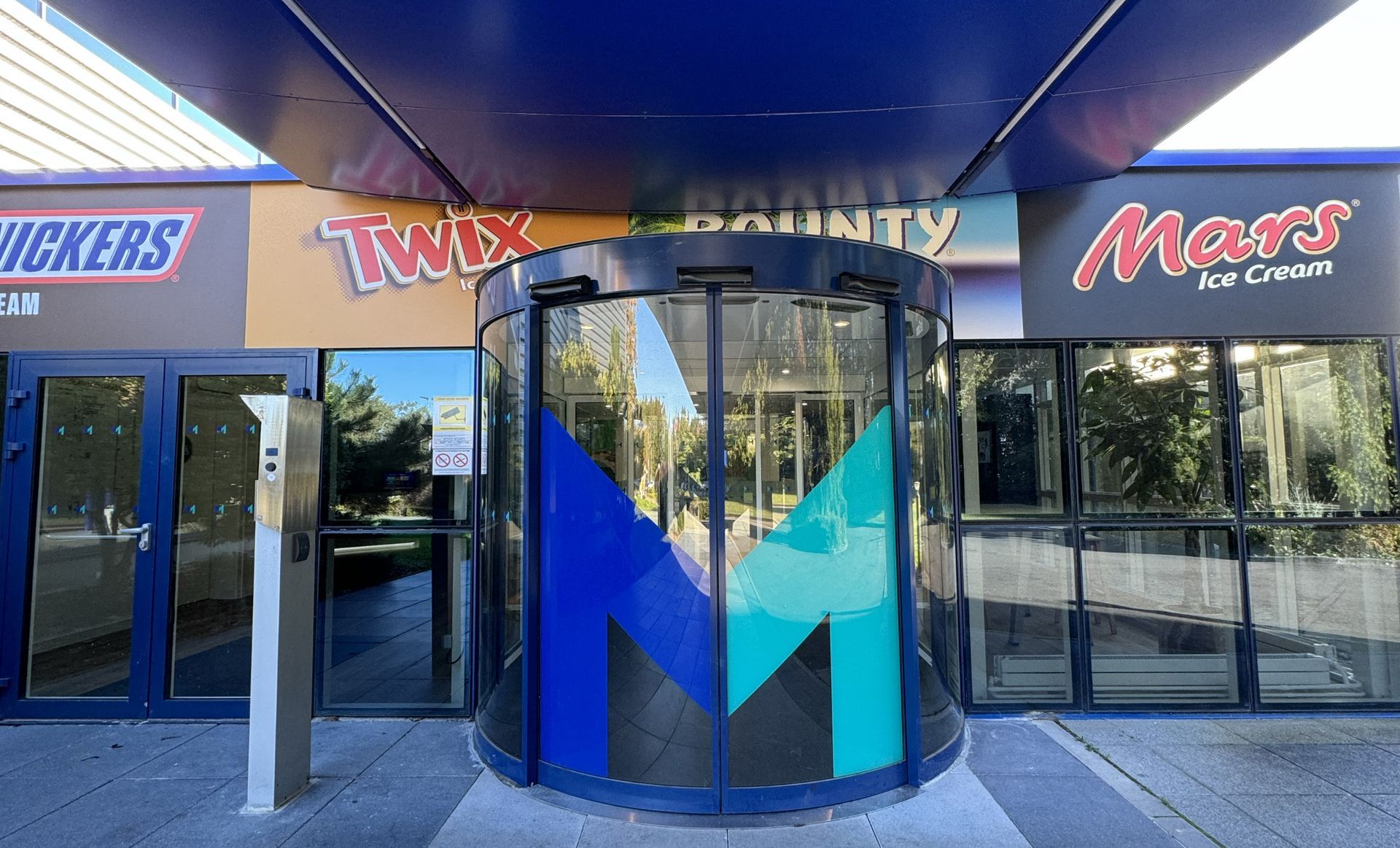 Entrance to a building with a revolving door and candy brand logos overhead: Snickers, Twix, Bounty, and Mars.