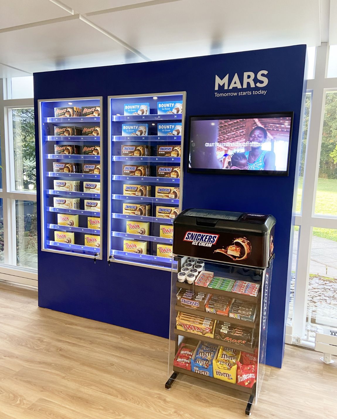 Mars candy display with lit shelves, a video screen, and a floor rack, all in blue and white.