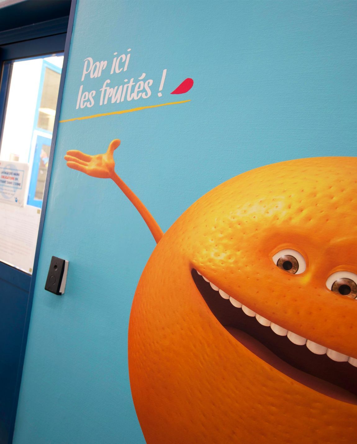 Orange cartoon character with a smile and outstretched arm on a blue wall. Text above reads 