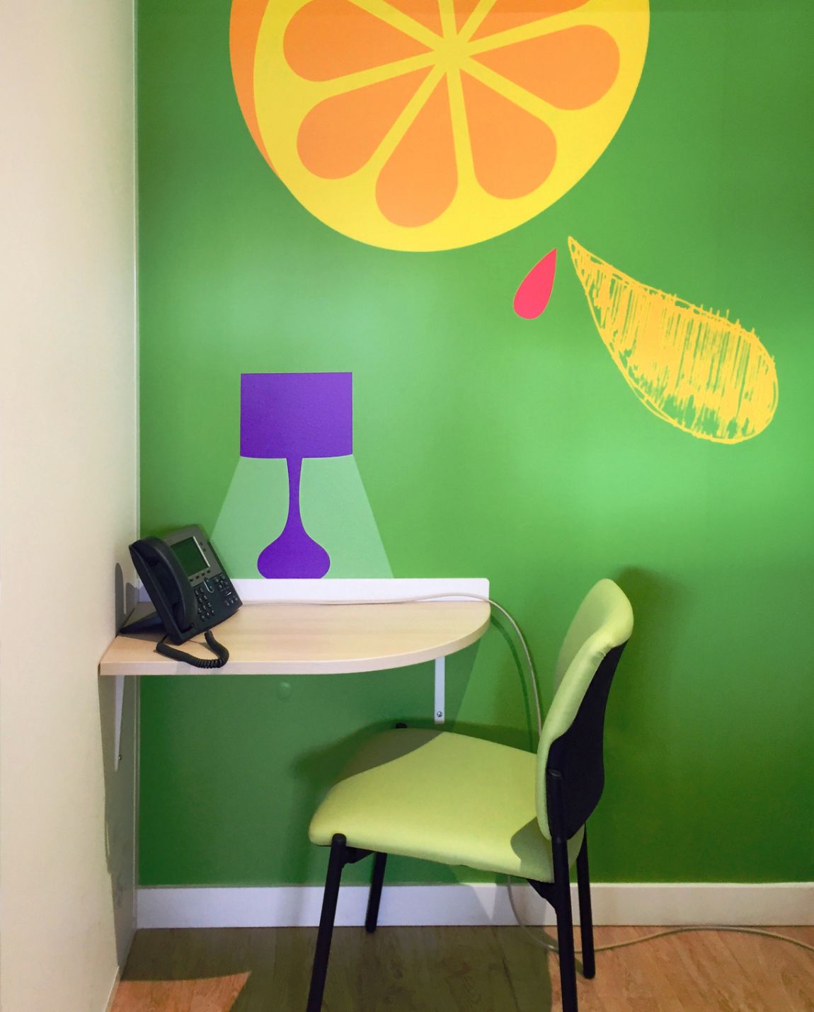 Desk and chair in front of a green wall with a citrus fruit design. Features a phone, lamp silhouette.