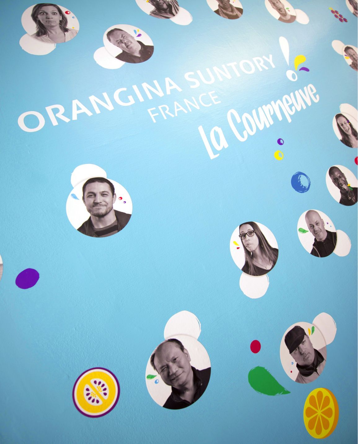Orangina Suntory France wall: People portraits in white circles, on a blue background with fruit accents.