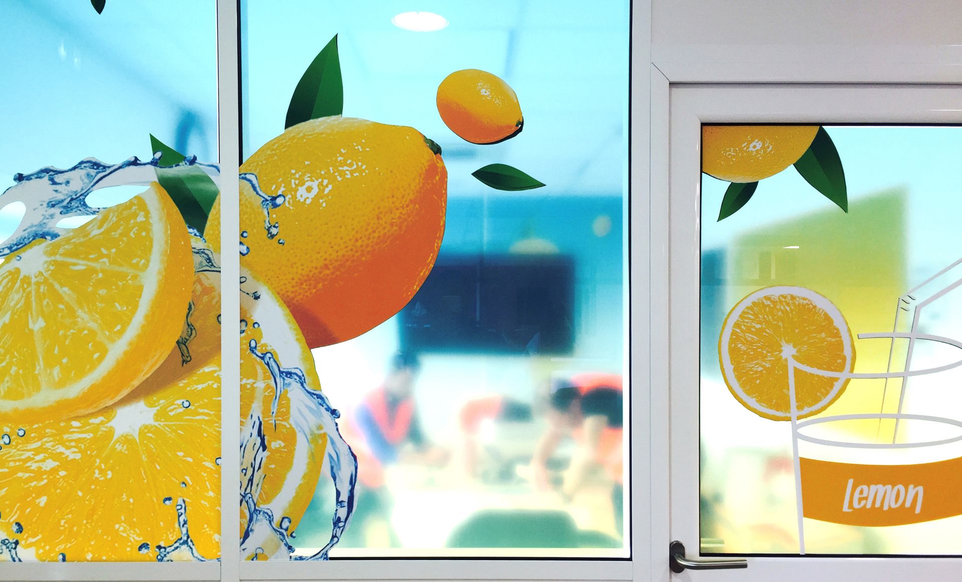 Lemon-themed window decals with lemons, leaves, and water splashes; a blurry interior with people is visible.