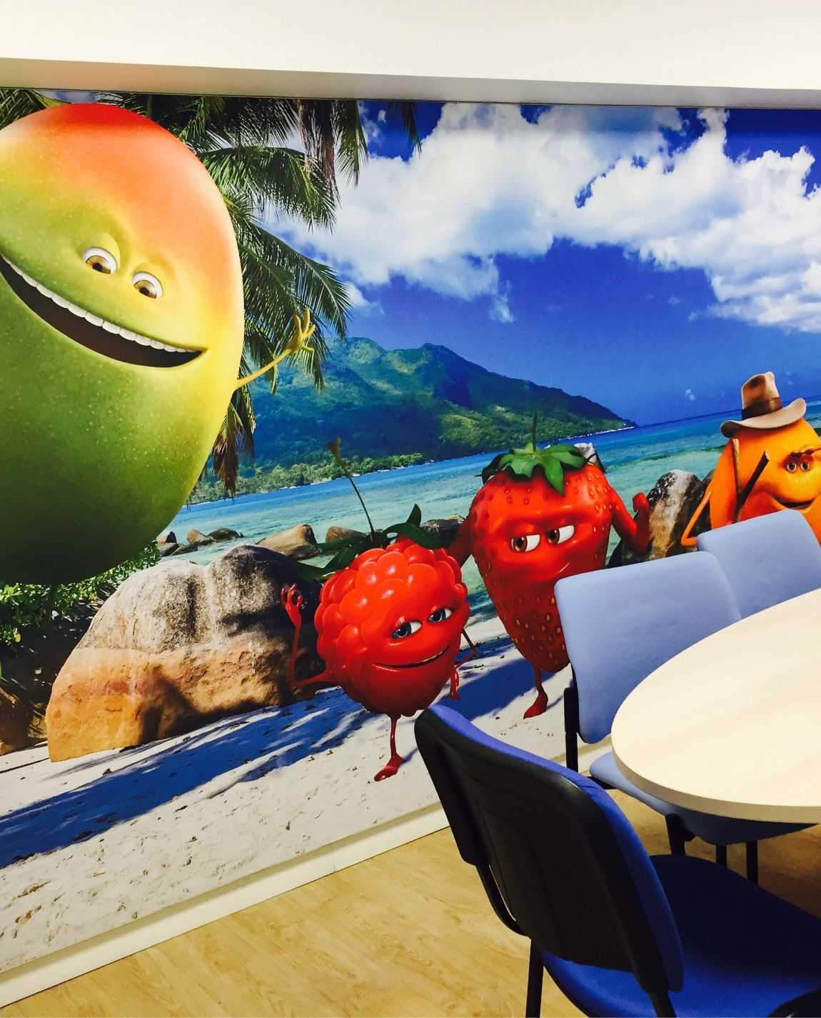 Wall mural with smiling mango, strawberries, and orange at a tropical beach setting.