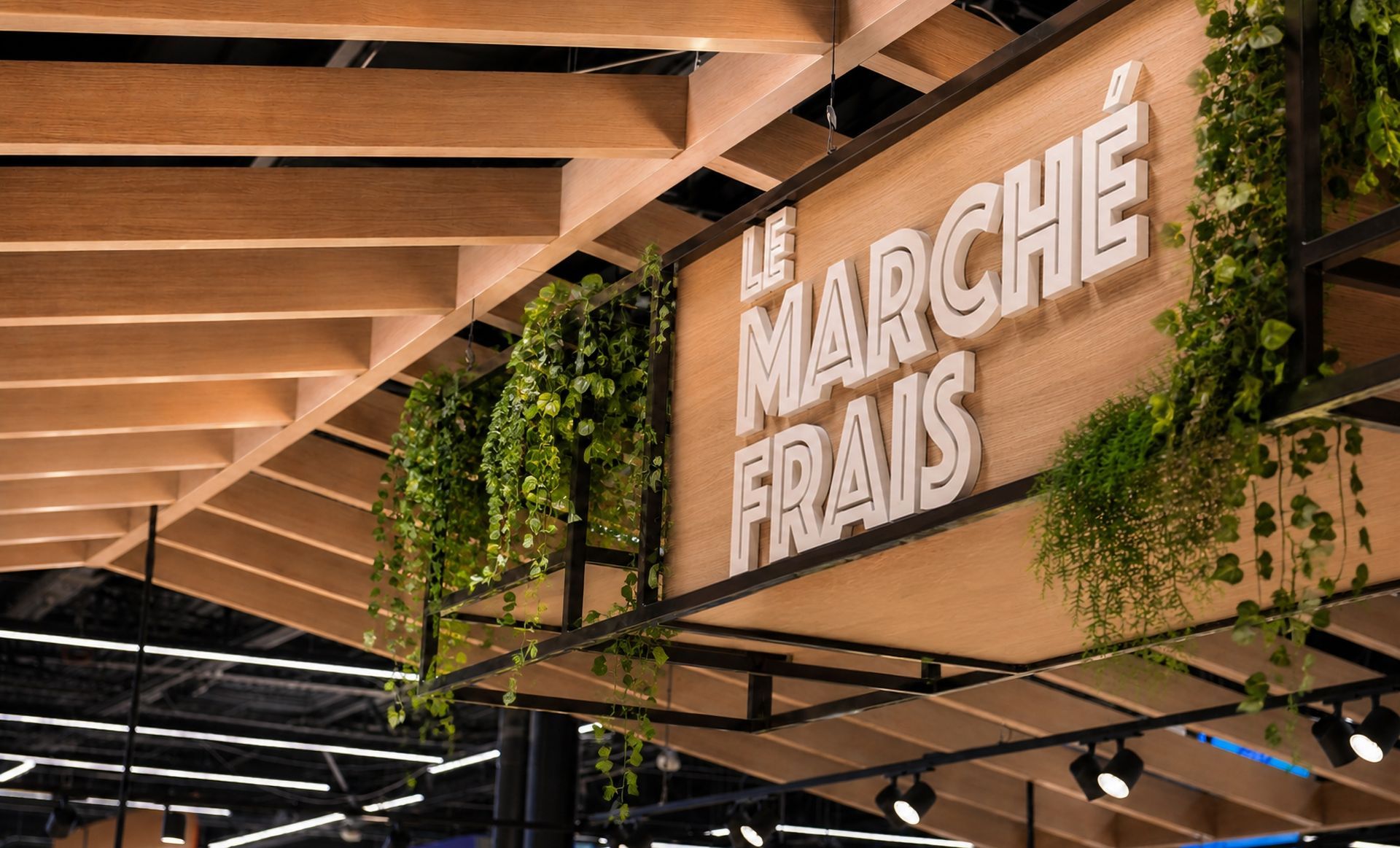 Enseigne intérieure DE SUPERMARCHÉ indiquant « Le Marché FraIS» sur une structure de plafond en bois et en métal