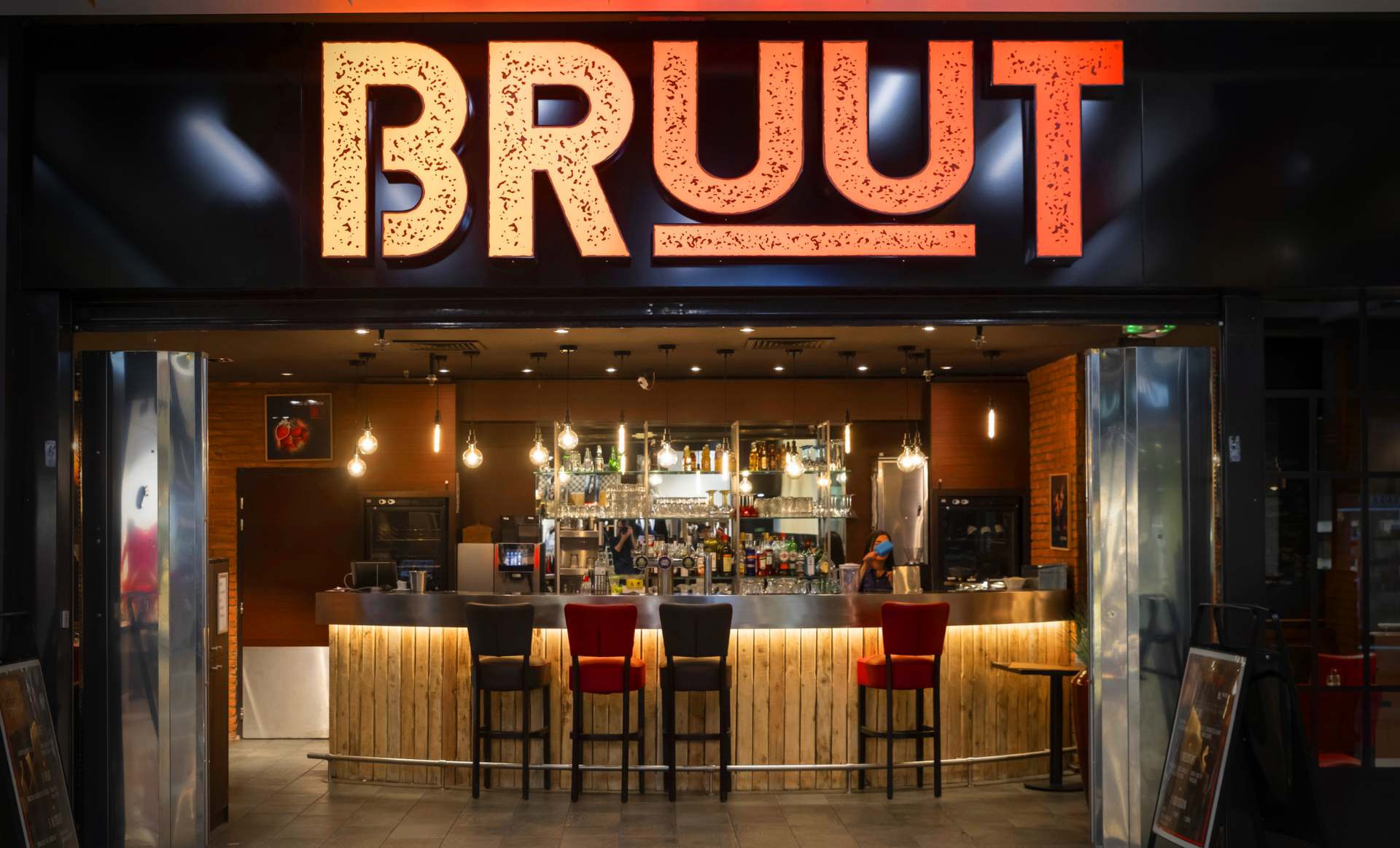 BRUUT restaurant exterior: illuminated sign, bar, bar stools.