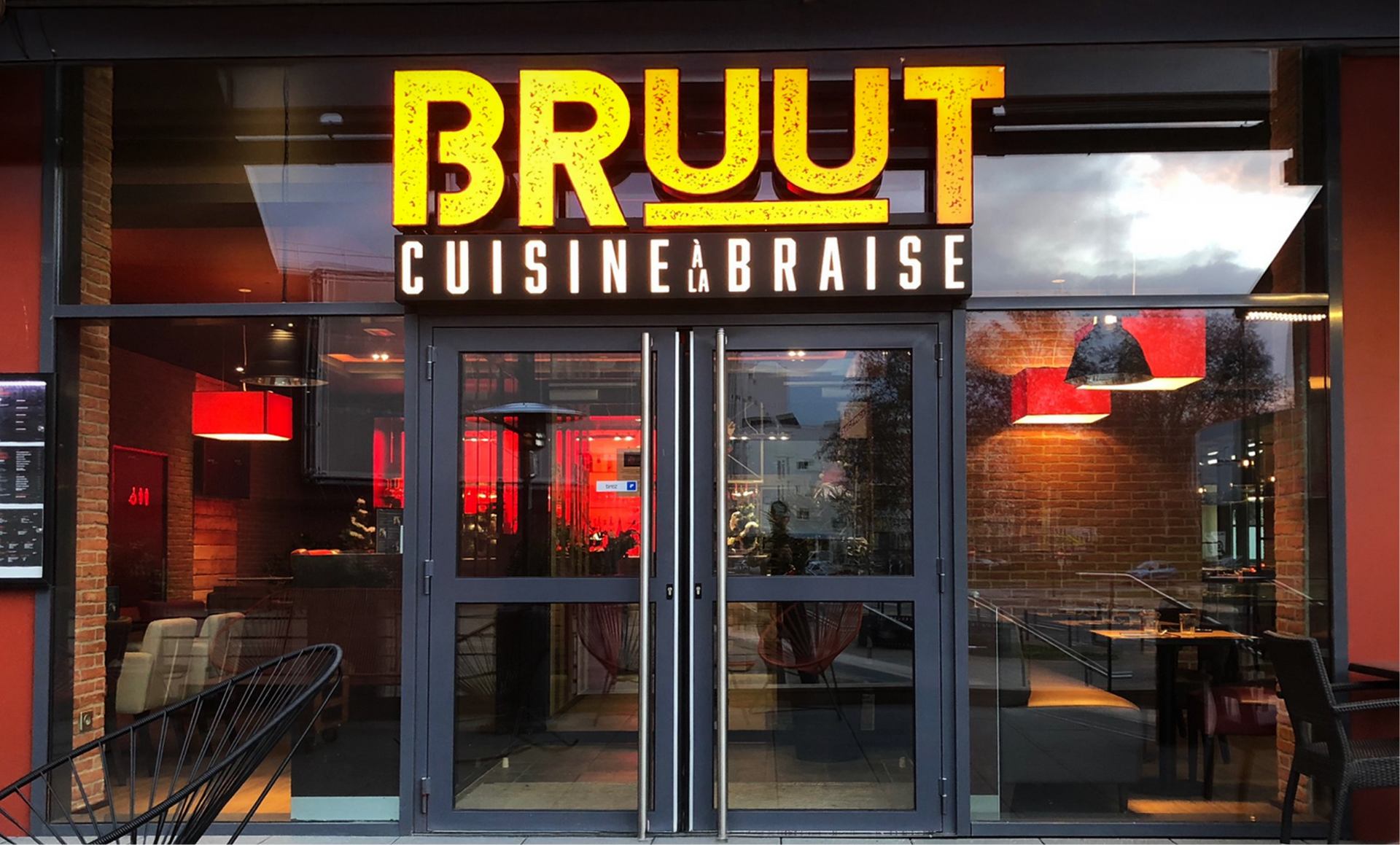 BRUUT Cuisine Braise restaurant entrance with illuminated sign, glass doors, and brick facade.