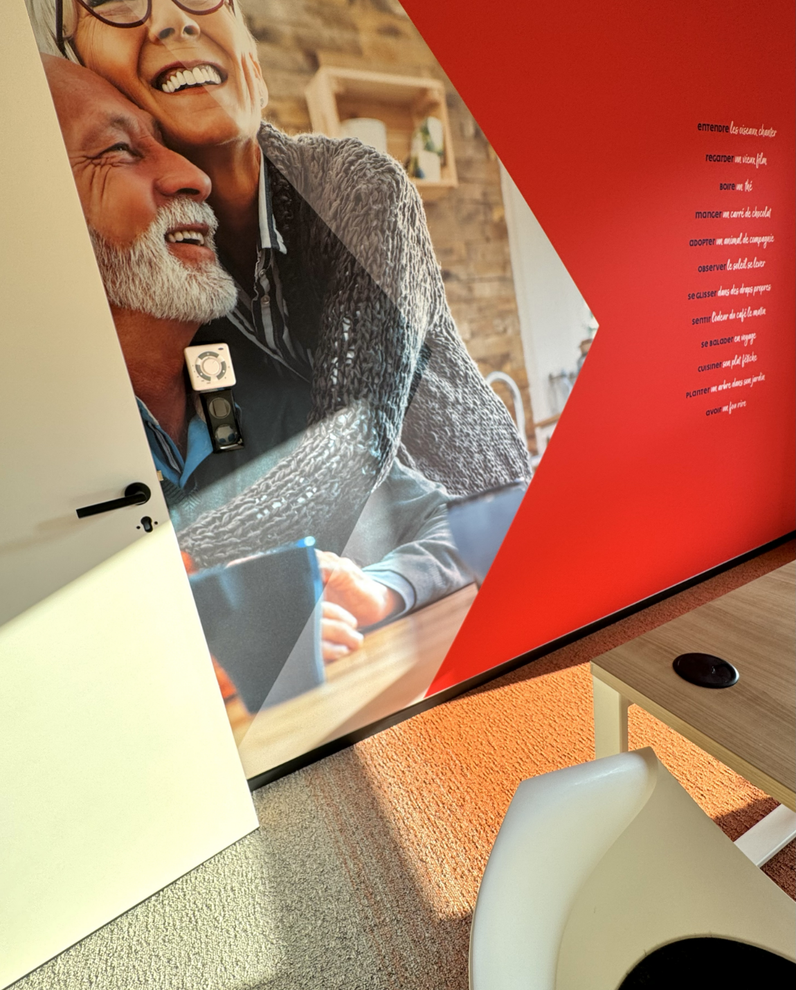 Elderly couple in a photo on a red wall, next to a door, table, and chair.