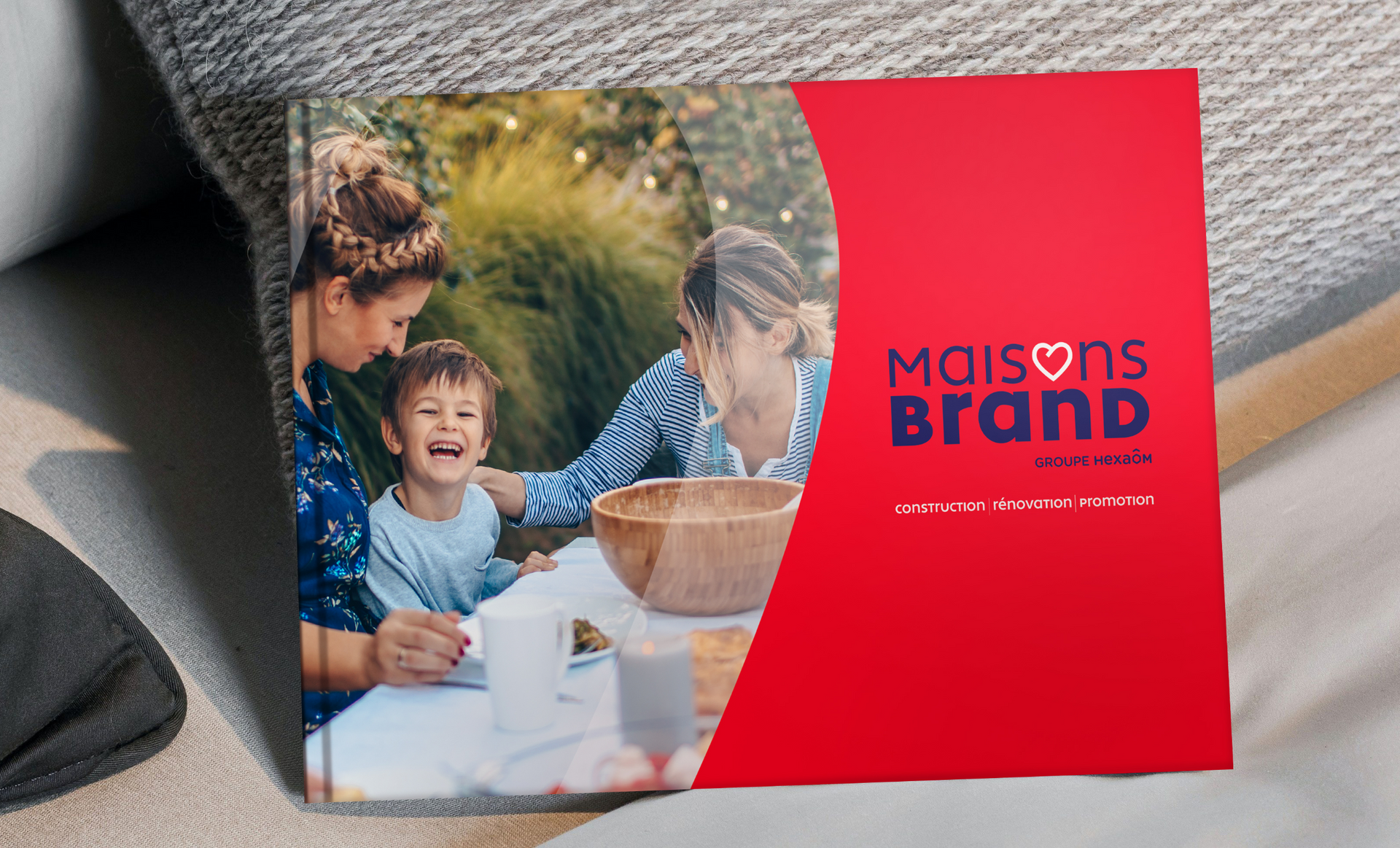 Photo album open on a couch. Family at a table. Red cover with logo