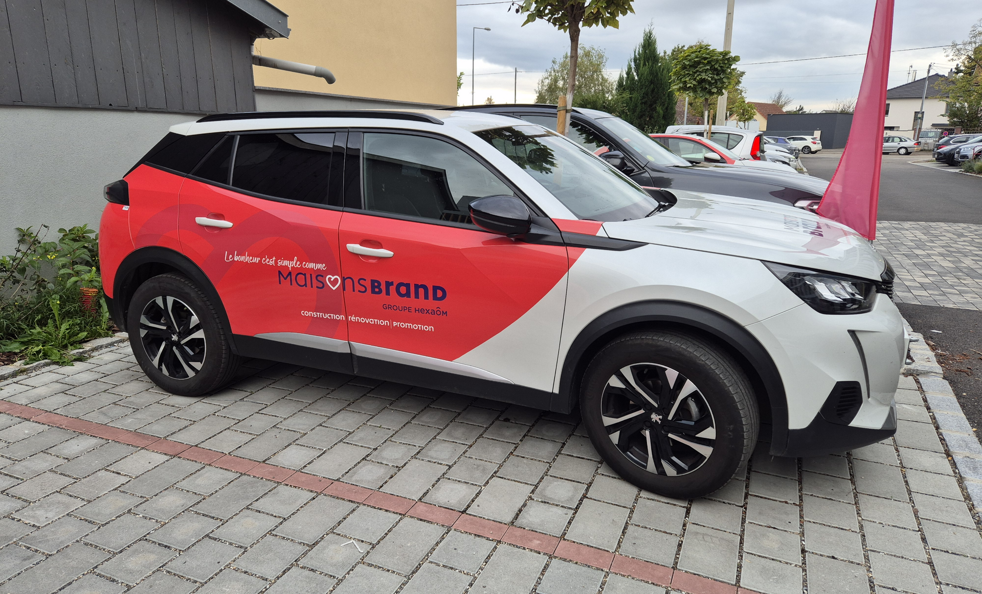 White and red SUV with advertising parked on cobblestones.