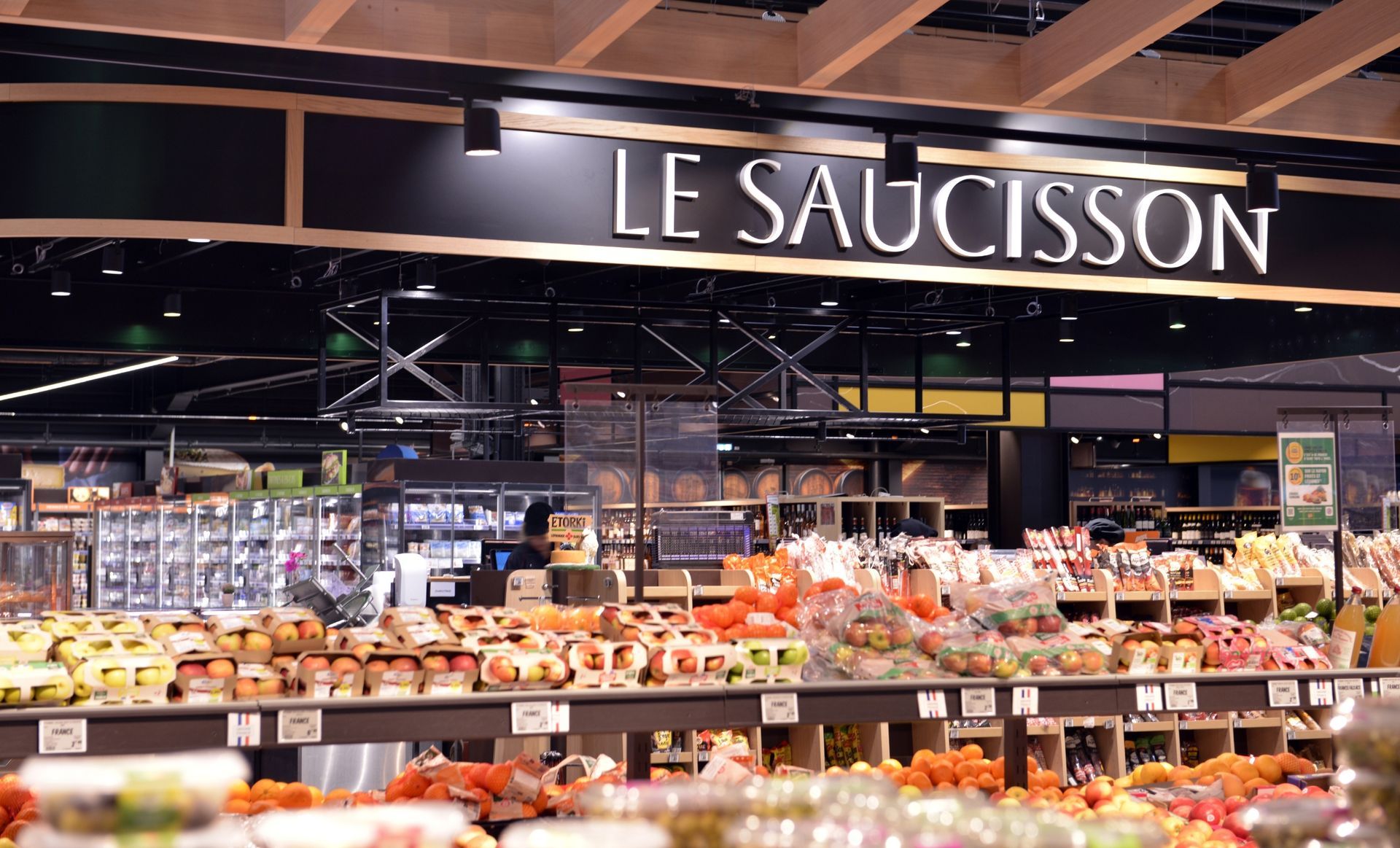 Comptoir de charcuterie avec des rangées de viandes et de fromages sous une enseigne indiquant « LE SAUCISSON »
