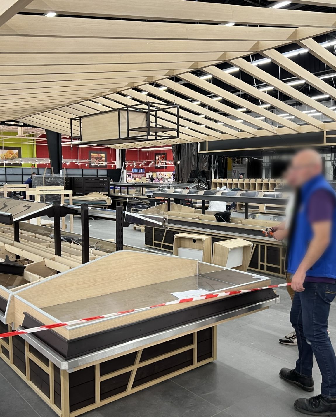 Allée d'un magasin de meubles avec des tables d'exposition et des panneaux rouges indiquant les soldes ; une personne floue marche sur la droite.