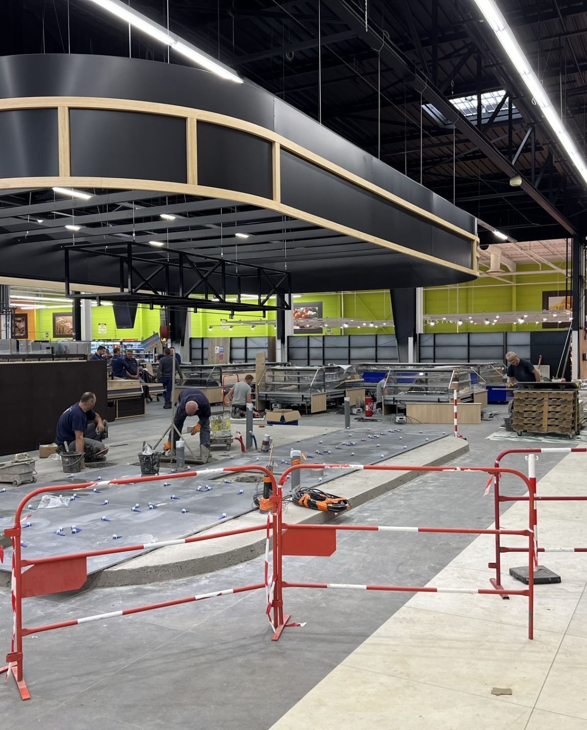 Chantier à l'intérieur d'un magasin avec des ouvriers, des barrières rouges et une grande structure de plafond incurvée en cours d'installation