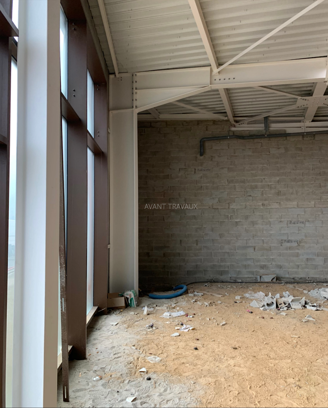 Interior construction site with unfinished walls and steel beams near a large window.