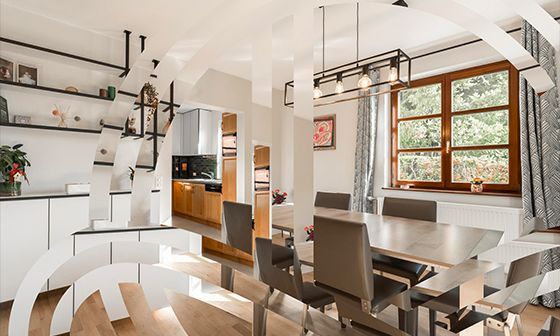 Dining room with table, chairs, window, kitchen in background, white cabinets, light wood floors.