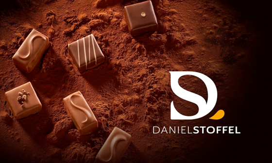 Assortment of chocolate candies on cocoa powder, with the Daniel Stoffel logo.