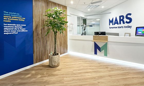 Mars company reception area. White counter, wood panel wall, plant, and the company logo on the wall.