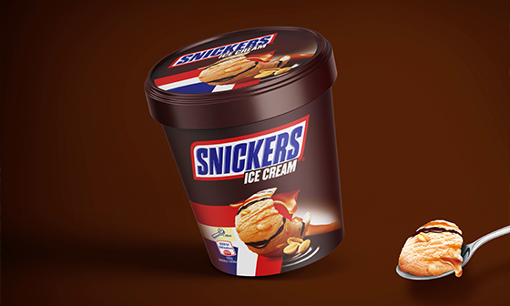 Snickers ice cream tub with a scoop on a spoon; brown background.