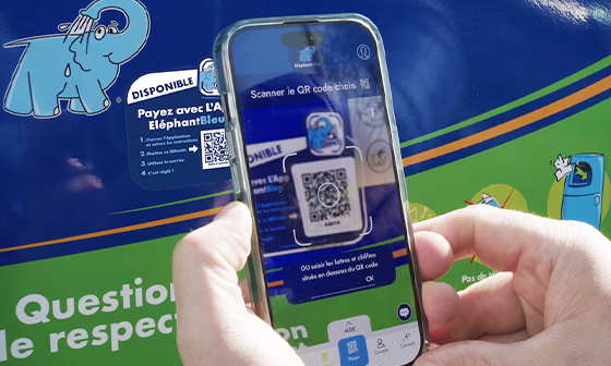 A person holding a phone scans a QR code on a recycling bin decorated with a blue elephant graphic.