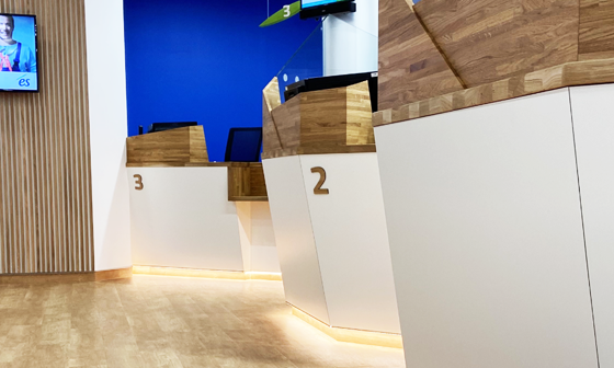 Guichets de banque modernes avec des accents blancs et de bois, numérotés 2 et 3, contre un mur bleu et lambrissé.