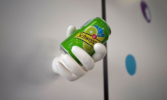 A green Schweppes can held by a white, hand-shaped wall decoration.