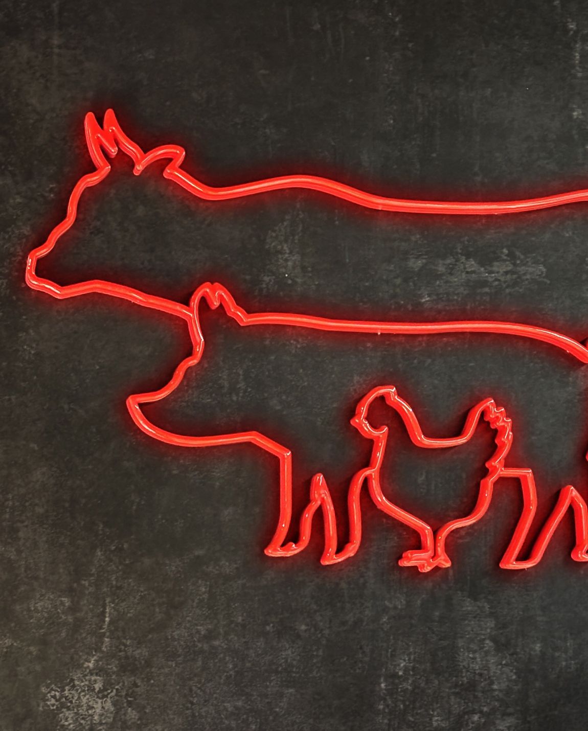 Silhouette rouge néon d'une vache, d'un cochon et d'une poule sur un mur sombre