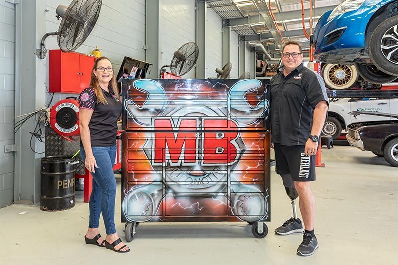 Man And Woman Standing Next To Each Other In A Garage Holding A Large Painting — MB Automotive In Garbutt, QLD